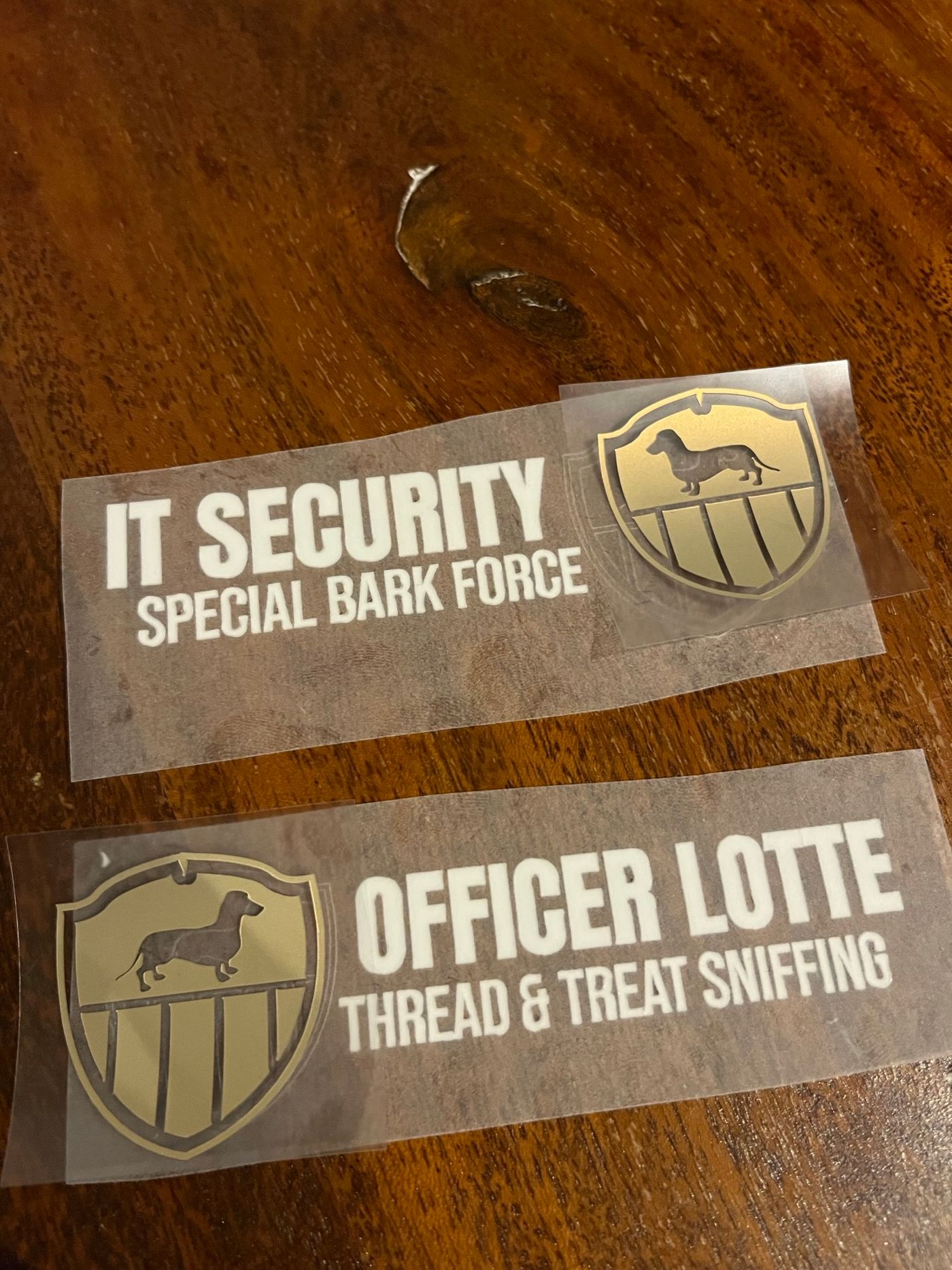 Goldfarbene Text-Transfers für eine Hunde-Uniform mit der Aufschrift Officer Lotte liegen bereit auf einem Holztisch.