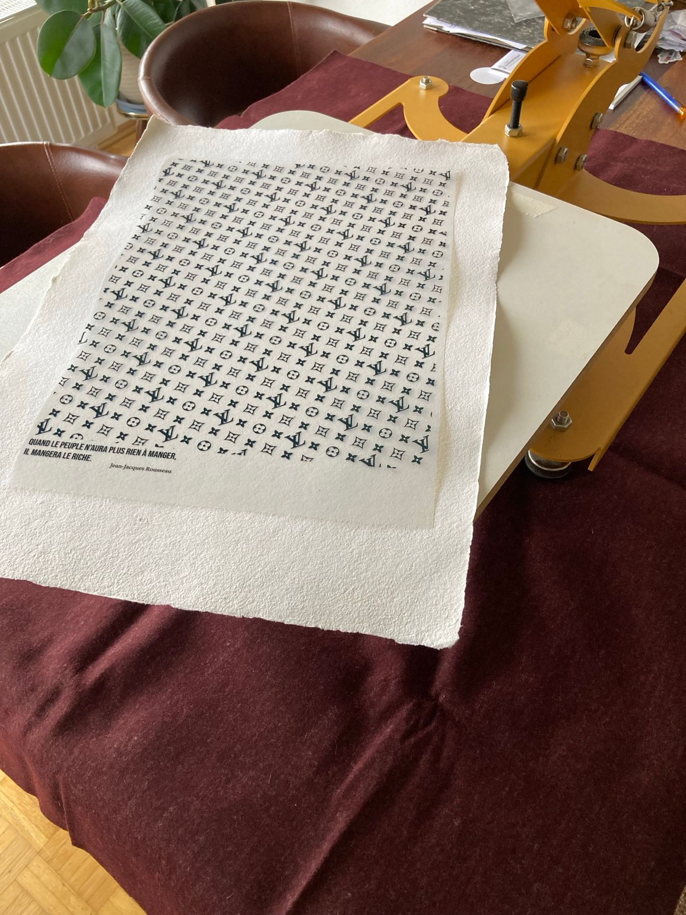 Ein edler Siebdruck in Olivgold auf handgeschöpftem Hahnemühle-Büttenpapier, platziert auf einem burgunderfarbenen Untergrund.